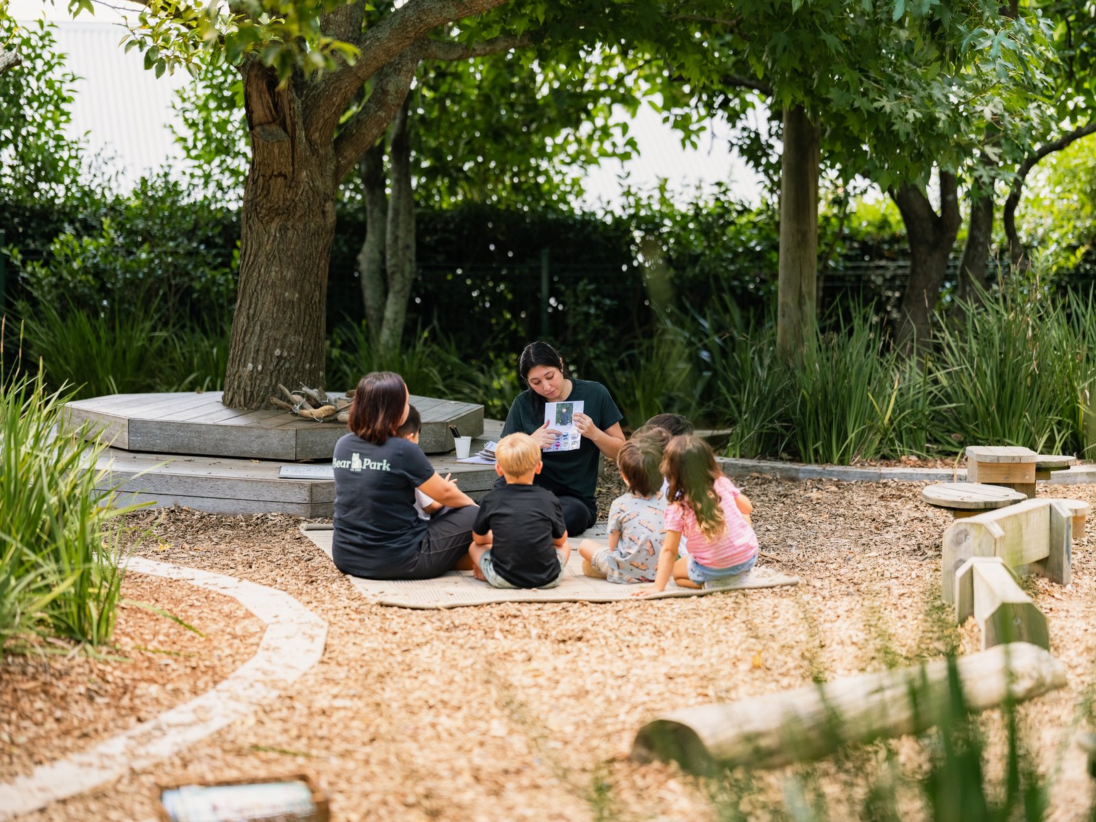 A teacher reading with children under the tree at Bear Park Epsom